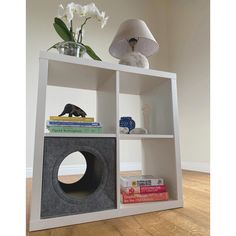 a white book shelf with books and a lamp on top of it in front of a wall