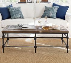 a living room with white couches, blue pillows and a coffee table in front of two windows