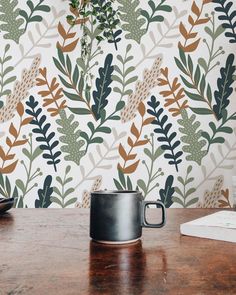 a wooden table topped with a coffee cup and plant wallpaper covered in green leaves