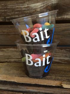 two plastic cups with different types of candy in them on a wooden table top, one has the word'bait'written on it