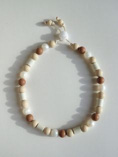 a white and brown beaded bracelet on a white surface with an orange charm hanging from it's end