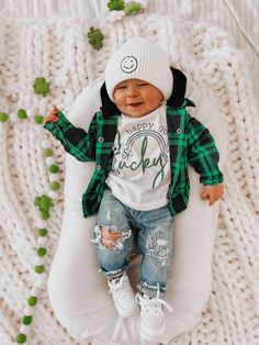 a baby is laying on a beanie while wearing jeans and a green plaid shirt