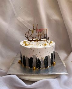 a white and black birthday cake with gold sprinkles is on a silver platter