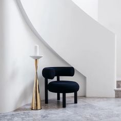 a black chair sitting next to a gold vase on top of a marble floor in front of a stair case