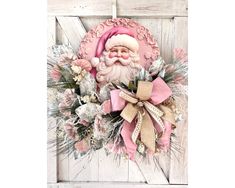 a pink and white christmas wreath with santa claus on it's face hanging from a wooden door