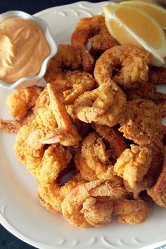 fried shrimp and dipping sauce on a white plate with lemon wedges next to it