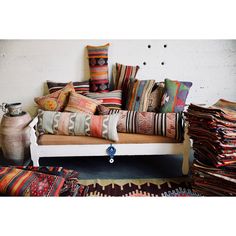 a couch with many pillows on top of it in front of a wall and rugs