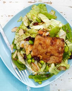 a blue plate topped with salad and meat next to a fork on top of a table