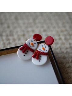 two snowmen wearing red hats and scarfs are sitting next to each other on a white surface