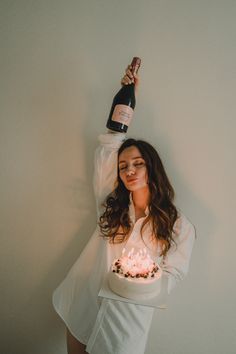 a woman holding a cake with candles on it and a bottle of wine above her head