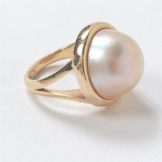 14K Yellow Gold Split Shank Mabe Pearl Ring Bezel set as the center feature is one (1) 17mm Mabe pearl with rose / cream color. Size 7.25 - 7.5 3mm 20mm x 20mm x 12mm 11.3 grams This item was appraised in March 2023 by Michael Bryant, Certified Gemologist Appraiser of Bryant and Sons, LTD. of Santa Barbara, CA.  (Picture of appraisal included in images). Please see pictures showing item details and condition. Elegant Wide Band Gemstone Jewelry, Timeless Oval Rings With High Luster, Wide Band Gemstone Rings For Formal Occasions, Formal Wide Band Gemstone Ring, High Luster Oval Yellow Gold Rings, High Luster Yellow Gold Oval Rings, Classic Dome Ring With Gemstone, Luxury Oval Pearl Ring With Polished Finish, Elegant Concave Gemstone Rings