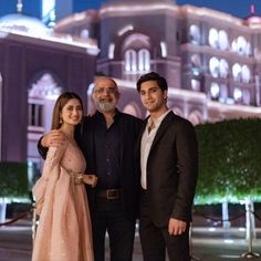 two men and a woman posing for a photo in front of a building at night