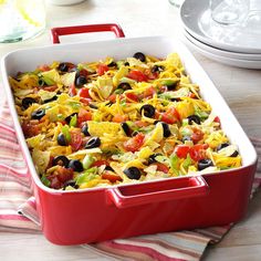 a red casserole dish filled with nachos and black olives