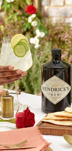 a person holding a bottle of gin on top of a table with flowers and napkins