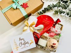 a person holding a christmas card next to a gift box and other holiday treats on a table