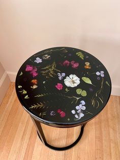 a black table with flowers painted on it and wooden floors in front of a white wall