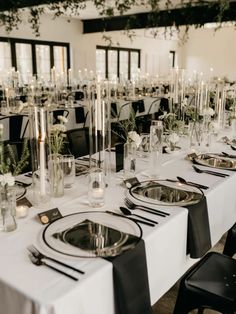 the tables are set up with black and white linens, silverware, and greenery