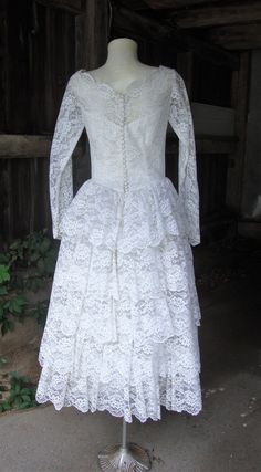 "This is a white lace and tulle full skirt wedding dress from the 1950's. The dress features a wide neckline with scalloped edges embellished with seed pearls and iridescent sequins. The sleeves are fitted and end in bridal points, opening with covered buttons and loops at the wrists. This dress opens down the back with covered buttons and loops and they are all there. The skirt is very full, with a multi tiered ruffled back. Under the lace layer is a full layer of tulle, and then an underskirt Vintage Wedding Dress With Attached Cancan, Vintage Lace Petticoat With Ruffles, Vintage Fitted Petticoat For Wedding, Vintage Fitted Wedding Petticoat, Tea Length Lace Trim Wedding Dress, Vintage Lace With Lace Bodice For Weddings, Vintage White Lace Dress For Wedding, Vintage Scalloped Lace For Wedding, Lace Ruffled Petticoat For Wedding