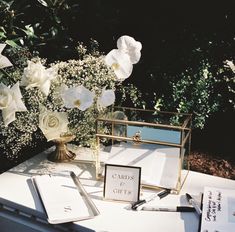 a table topped with white flowers next to a vase filled with water and writing utensils