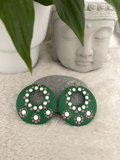 two green and pink earrings sitting on top of a white rug next to a potted plant