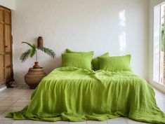 a bed with green sheets and pillows in a room next to a plant on the floor