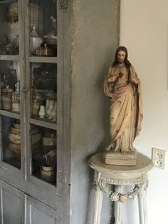 a statue of jesus on top of a table next to a book shelf and cupboard