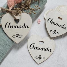 three wooden hearts with names on them sitting next to some dried flowers and a blue cloth