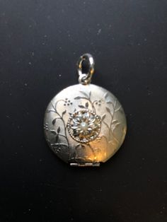 1950s brushed and etched silver tone locket: This sweet dual photo locket has a brushed and etched surface with a floral design. It is centered with a bloom which is in turn centered with a glass pearl. It is  1 1/8 in. in diameter. Vintage Silver Flower Pendant Jewelry, Vintage Medallion Jewelry With Flower Charm, Vintage Silver Jewelry With Flower Pendant, Vintage White Gold Medallion Locket Necklace, Vintage Silver Flower Pendant Locket Necklace, Silver Elegant Locket Necklace With Flower Charm, Elegant Silver Locket Necklace With Flower Charm, Silver Locket Necklace With Flower Charm As Gift, Vintage Silver Etched Locket Necklace