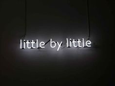 a neon sign that says little by little in the middle of a dark room with strings hanging from it