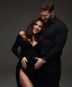 a man and woman are posing for a photo in front of a gray background with their arms around each other