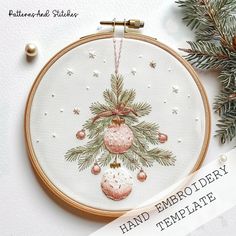 an embroidered christmas ornament hanging from a hoop with pine branches and ornaments on it