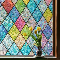 a vase filled with yellow tulips sitting next to a colorful stained glass window