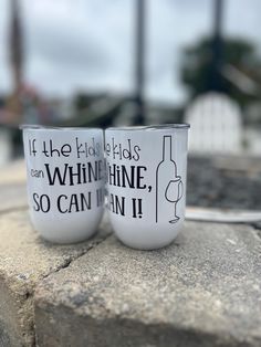 two white coffee mugs sitting on top of a stone wall next to each other