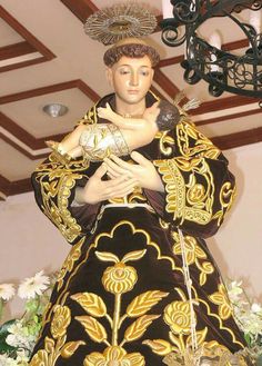 a statue of a woman wearing a black and gold dress with flowers in the background