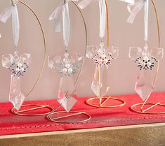 four glass ornaments are sitting on a red tablecloth with gold wire and ribbons hanging from them