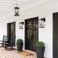 a black rocking chair sitting on top of a porch next to two potted plants