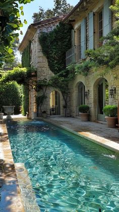 an outdoor swimming pool in front of a stone building with potted plants on the side