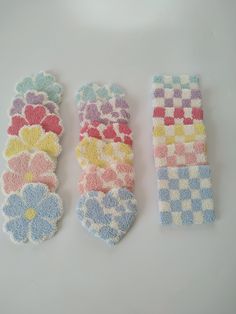 three pieces of colorful knitted fabric with flowers and hearts on them are laid out side - by - side