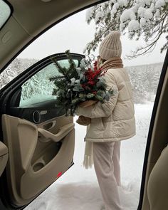 a woman is getting out of her car in the snow and holding a christmas wreath