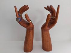 two wooden hand sculptures with rings on their fingers, one holding the other in the air