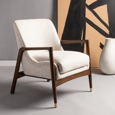 a white chair sitting in front of a painting on the wall next to a vase