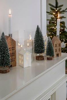 small christmas trees and candles on a mantle in front of a decorated fireplace mantel