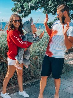 a man and woman standing next to each other near the ocean with one holding a small child