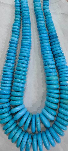 two blue beads are hanging from a necklace on a white surface with sand in the background