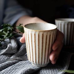 a person holding a white cup on top of a blanket