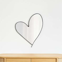 a heart shaped mirror hanging on the wall above a dresser with drawers in front of it