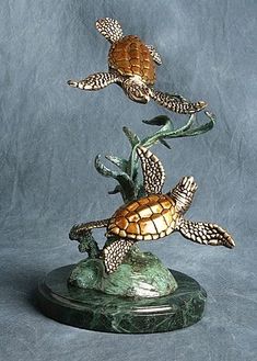 three sea turtle figurines are on top of a green marble base and one is in the air