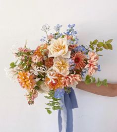 a person holding a bouquet of flowers in their hand and wearing a blue ribbon around it