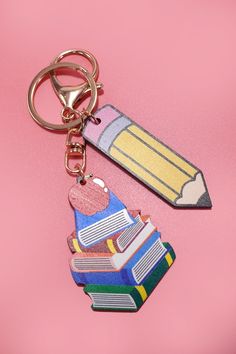 a pencil and book shaped keychain on a pink background