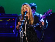 a woman singing into a microphone while standing next to a keyboard and amp on stage